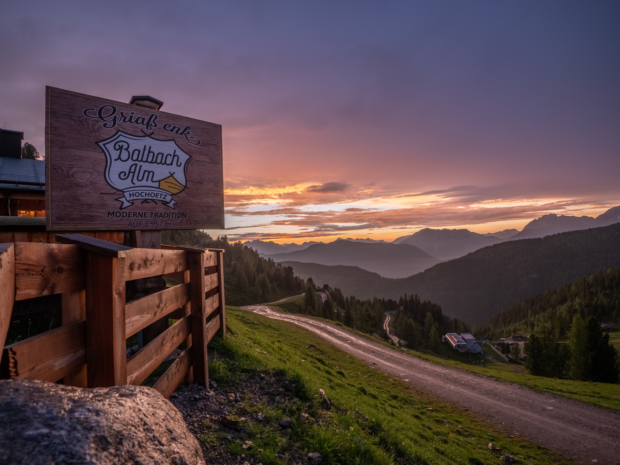 Ein Foto eines Holzschildes der Balbach Alm bei Sonnenuntergang mit der Bergkulisse im Ötztal im Hintergrund